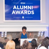 President Mantella talking to crowd with 2024 Alumni Awards image in the back